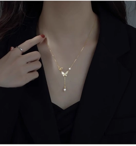 Detailed close-up of a gold butterfly necklace with zircon stones and a single white pearl