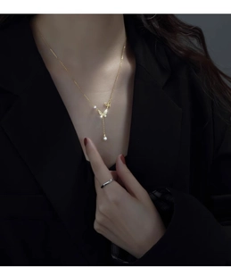 Detail of a golden butterfly necklace with zircon stones and a pearl on a model's neck