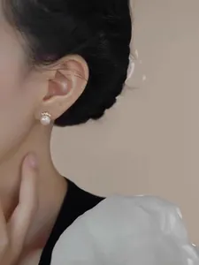 Close-up of white round pearl earring with gold crown accent on model's ear