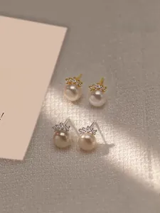 Macro shot of crown-shaped diamond and pearl earrings in gold and silver finishes