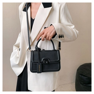 Detail of black square handbag with metal buckle and adjustable shoulder strap on white suit