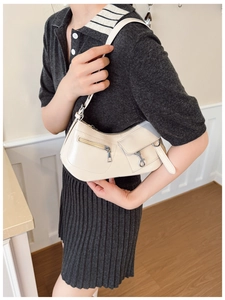 Detail shot of a cream-white underarm bag with silver zippers and buckle on the strap