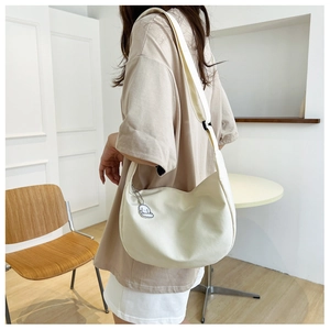 Détail du sac à bandoulière blanc cassé avec breloque et large sangle réglable