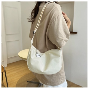 Détail du sac demi-lune en toile blanc cassé avec pendentif et bandoulière