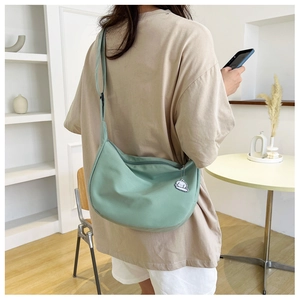 Détail d'un sac bandoulière en toile vert menthe avec un pendentif de personnage de dessin animé