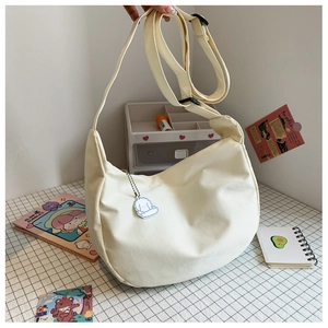 Détail du sac à bandoulière demi-lune blanc cassé en toile avec sangle réglable et bijou