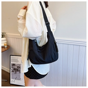 Vista lateral de un bolso bandolera de nailon negro en forma de medialuna en un modelo