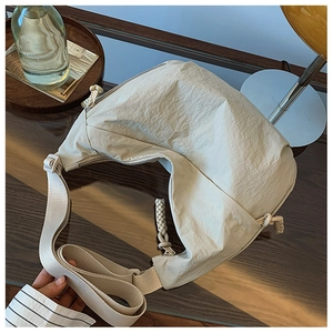 Detalle de cerca del bolso de media luna en nailon beige arrugado sobre mesa de cristal