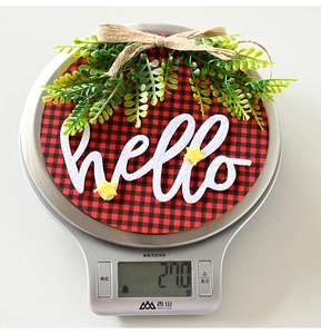Detail of round Buffalo plaid Christmas door sign with hello text and green leaves