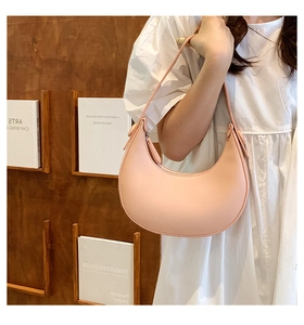 Close-up of minimalist apricot half-moon shoulder bag worn by a model in white dress