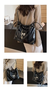 Dettaglio borsa tote in pelle verniciata nera con fiocco bianco e tracolla a catena