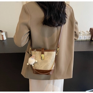 Detail van een tweekleurige bucket bag met gouden sluiting en een zachte pluche hanger