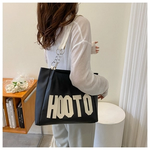 Detail of black and white tote bag featuring HOOTO logo and wide white shoulder strap