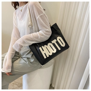Detail of a black leather tote bag featuring bold white HOOTO print and metal chain handle