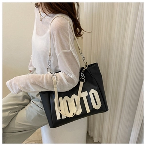 Detail of black tote bag with white HOOTO lettering and metal chain shoulder strap