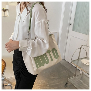 Detail of large canvas tote bag featuring green HUOTO lettering and chain strap accents