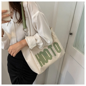 Detail of green HOOTO embroidered letter on off-white canvas tote bag with shoulder strap