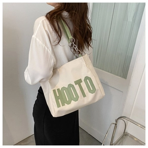 Detail of a large cream canvas tote bag with green HOOTO lettering and metal chain