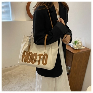 Detail of canvas tote bag featuring brown HOOTO applique and metal chain leather handle