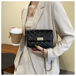 Schwarze Mini-Stepptasche mit goldener Kette am Modell in einem beigen Blazer