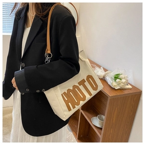 Close-up of a canvas tote bag with brown straps and HOOTO letter embroidery