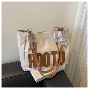 Detail of beige tote bag with HOOTO patch, brown leather strap and silver chain link