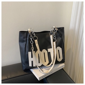 Detail of black tote bag with HOO10 college style patch and metal chain strap
