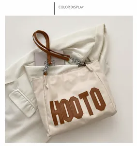 Detail of khaki tote bag featuring large HOOTO patch and metal chain shoulder strap