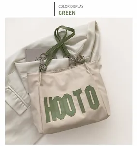 Detail of white tote bag with green HOOTO embroidery and chain strap on white blazer