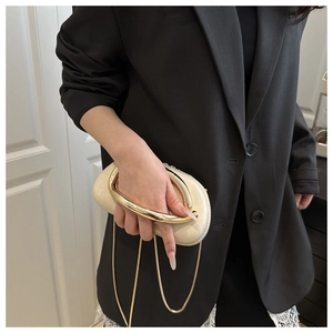 Detail of cream oval clutch bag featuring a chunky gold metal ring handle and fine chain