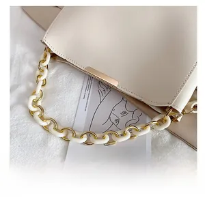 Détail du sac seau beige clair montrant la poignée en acrylique blanc et chaîne dorée