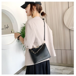 Détail d'un sac seau noir élégant avec chaîne dorée sur mannequin dans un café chic
