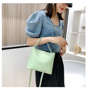 Détail du sac seau vert menthe avec anse chaîne porté par un mannequin en jean bleu