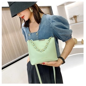 Détail du sac seau en cuir vert clair avec chaîne dorée et logo de mode élégant