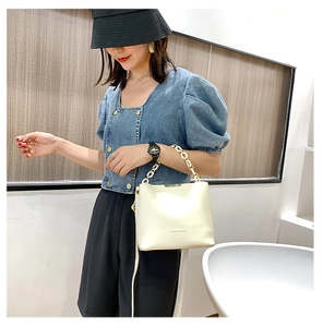 Détail du sac seau blanc en cuir PU avec une large chaîne décorative dorée et blanche