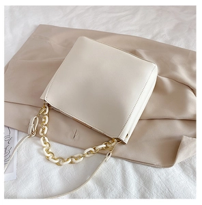 Détail d'un sac bandoulière crème avec chaîne dorée et résine sur fond de soie douce