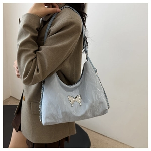 Detail of light blue pleated shoulder bag with a silver butterfly ornament and metal chain