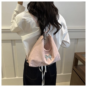 Detail of light pink shoulder bag with a silver butterfly ornament on a textured surface