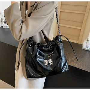 Dettaglio borsa shopper nera lucida con coulisse, fiocco argento e tracolla a catena
