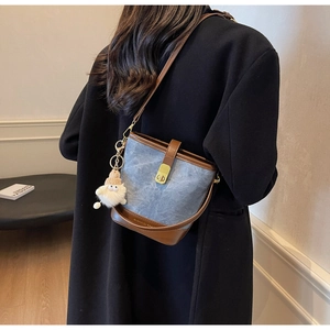 Model draagt een denim emmertas met bruine lederen bies en schattige pluche hanger