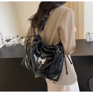Dettaglio borsa tote in pelle verniciata nera con catena d'argento e fiocco in metallo