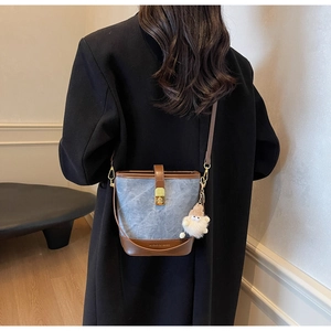 Detail van blauwe denim emmertas met bruine lederen afwerking en schattige pluche hanger