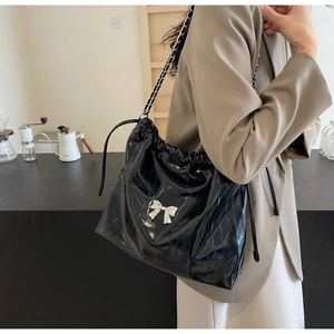 Dettaglio borsa tote in pelle verniciata nera con fiocco in metallo argento e catena