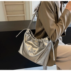 Dettaglio borsa tote argento con catena e coulisse indossata su un blazer verde scuro