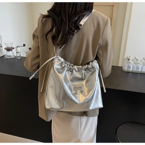 Borsa tote argentata con catena e fiocco indossata da una modella in un caffè moderno