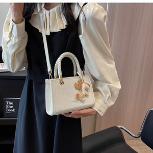 Detail of white embossed leather tote bag with woven handle and horse charm accessory