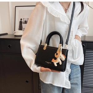Detail of black stone-pattern handbag with braided handle and cute horse charm