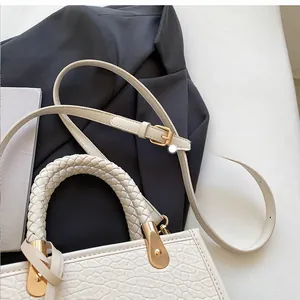 Detail of cream leather tote bag featuring woven handle and gold hardware on grey suit