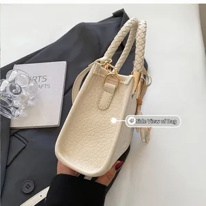 Side view of cream crocodile pattern handbag with braided handle and gold hardware