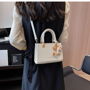 Detail of white crocodile pattern tote bag with woven handle and orange horse charm